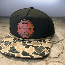 Load image into Gallery viewer, Black cap with camouflage brim and 'War by the Shore' logo on a stone surface
